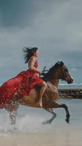 Beautiful woman horseback riding on the beach in flowing red dress, splashing in the water, cinematic slow motion