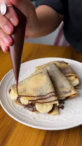 Banana Nutella Crepes🍫🍌 I love a good crepe recipe and this one's my favourite for so many reasons. Easy, buttery & wonderful! This recipe is so versatile, you can eat it as it is or have it with any of your favourite toppings ~ mine is with banana and lots of Nutella! Here's how you make these delicious Banana Nutella Crepes at home 😍 ▶️ Ingredients : Refined flour/ Maida - 1/2 Cup Whole Wheat flour/ Atta - 1/2 Cup          Oil - 1 Tbsp Salt - 1/2 Tsp Milk - 3/4th Cup Water - 1/2 Cup + 1 tbsp Sugar - 2 Tbsps Butter - 1 Tsp per crepe Banana & Nutella ▶️ Process: * Crepe batter : To a blender, add in whole wheat flour, refined flour, oil, salt, sugar, milk & 1/2 of the water - blitz until combined * Strain the batter in a bowl & set aside for at least 20 mins * Once the batter has rested, add in the rest of the water & give it a good mix - your crepe batter is ready * To make the crepe, heat up some butter in a nonstick pan, pour a ladle of the batter onto to pan & swirl it around until the batter covers the pan completely - cover the pan with a lid * Allow the crepe to cook on one side on low heat for 2 mins/ until the sides start to shrink * Flip it over & repeat the same process - this batter makes 6 crepes * To Assemble : apply a generous layer of nutella on half of the crepe & top it up with sliced bananas - fold the crepe as shown in the video * Finish the crepes with a generous drizzle of heat for 2 mins/ until the sides start to shrink * Flip it over & repeat the same process - this batter makes 6 crepes * To Assemble: apply a generous layer of nutella on half of the crepe & top it up with sliced bananas - fold the crepe as shown in the video * Finish the crepes with a generous drizzle of nutella along with a dusting of icing sugar & Enjoy Happy Cooking 😍 #Nutella #crepe #banana #nutellacrepe #dessert #chocolate #hazelnut #cooking #baking #brunch #explore #trending #fypシ #fyp #foryou #foryoupage #trend #viral #tiktok 