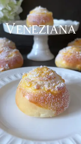 Veneziana Recipe 🤍 The delicate dough balls, filled with a delicious pudding cream and sprinkled with crispy pearl sugar, are a true delight 🥰🤍 📝 Ingredients:  (For 17 pieces)   For the pre-dough: - 175 g all-purpose flour (Type 405) - 150 ml lukewarm milk - 5 g fresh yeast   For the main dough: - The prepared pre-dough - 300 g all-purpose flour (Type 405) - 125 ml lukewarm milk - 60 g sugar - 60 g soft butter - 1 egg - A pinch of salt   For the filling and decoration: - 200 ml milk - 15 g cornstarch - 35 g sugar - 2 egg yolks - 1 teaspoon vanilla extract  - 1 egg yolk whisked with 1 tablespoon cream or milk  - Pearl sugar for sprinkling  🤍 Preparation: 1. In a bowl, mix flour, lukewarm milk , and yeast for the pre-dough. Cover and let it rise in a warm place for about 30 minutes. 2. Add flour, lukewarm milk, sugar, soft butter, egg, and a pinch of salt to the pre-dough. Knead everything into a smooth dough. 3. Cover the dough and let it rise in a warm place for about 1 hour, until it doubles in volume. 4. In a pot, heat milk, cornstarch, and sugar while stirring egg yolks until the mixture thickens. Add vanilla extract. Remove from heat and let it cool. 5. Shape the risen dough into 17 small balls (50 g each) and place them on a baking sheet lined with parchment paper. Let the dough balls rise slightly. 6. Brush the dough balls with an egg yolk-cream or egg yolk-milk mixture. 7. Place pudding strips on the dough balls. 8. Sprinkle pearl sugar generously over the pudding strips. 9. Preheat the oven to 180 degrees Celsius and bake the dough balls for about 15-20 minutes until they are golden brown. 10. Remove from the oven, let them cool completely, and generously sprinkle with powdered sugar. Enjoy these delicious Veniziana as a sweet temptation for in-between moments! 🥰🤍