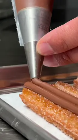 Valentine's Special: Keeping her wet for more. #churros #dessert #churrodessert #strawberry #whippedcream #ValentinesDay #forher  Here, we have beautiful churro sticks finished with Nutella and icing sugar. With Nutella, you can skip the whole chocolate sauce aspect. What I also love about these is that they are simple to make and easy to cook. It can also be made in advance. The trick for a good shape is to semi or fully-freeze them. Recipe instructions are below. Before you begin:  1. Dress to impress, stay classy, and respect consent.  2. If you don't have the budget, there is no need to go overboard with flowers (it's the thought that counts, amigo). 3. For more tips, check my recipe site. Serves 2 (12 -15 sticks at 20-22 cm (+-) depending on your final nozzle tip and preferred length) Difficulty – Easy Tools: 2x Piping bags (or reusables), 11mm-15mm star tip nozzle for churros, 6mm round tip for Nutella garnish, oil temp thermometer (not necessary but ideal), parchment paper. Recipe: - 17g sugar - 3g sea salt - 48g butter - 188g water - 1 egg - 113g flour - 1 tsp vanilla essence or sugar - 1-2 litter frying oil - Punnet of strawberries + touch sugar and/or seedless raspberry jam & whipped cream - ½ btl champagne (optional) - 3 roses (optional) - Small Jar of Nutella (you won't need all of it) - Sugar + Touch of Cinnamon sugar to coat - Icing sugar for garnish Steps to Sucess: Add water, sugar, butter, salt, and vanilla extract in a pot over medium-high heat. Once thoroughly melted and it starts to boil, add flour and whisk in vigorously. Continue cooking dough until it comes away from the pan. Take off the heat, and place the dough in a large bowl. Allow to cool until warm to touch. Add one egg and immediately whisk in until fully incorporated. Place into a piping bag and pipe onto a prepared baking sheet over a tray. Place in the freezer until it's semi-frozen (it starts almost to hold its shape as a stick as you pick it up). Fry at 350°F/176.667°C until golden brown. Once cooked, place over a rack over a tray to allow excess oil to drip off—coat in cinnamon sugar. Garnish with piped Nutella. Serve with strawberries, cream, and your choice of drink and flowers.