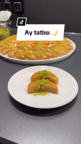 Ay tatlısı  Malzemeler:  125gr tereyağı  2 yumurta birinin sarısı üzeri için  Yarım çay bardağı irmik  Yarım çay bardağı şeker  Yarım çay bardağı yoğurt  Yarım çay bardağı sıvı yağ  1 paket kabartma tozu  2 yemek kaşığı sirke  1 çay bardağı çekilmiş ceviz  3,5 su bardağı un  Şerbeti için: 2,5 su bardağı şeker  2,5 su bardağı su  1 dilim limon  Yapılışı  Ay tatlısı hamuru için karıştırma kabına tereyağı,sıvı yağı,yoğurt, irmik, sirke,şeker,yumurta, ceviz ve kabartma tozunu alalım ve elimizle karıştıralım. Kontrolü bir şekilde unu da ekleyerek hamurumuzu yoğurmaya başlayalım.  Yumuşak kıvamda bir hamur elde edelim. Hamurumuz hazır olduktan sonra bir kenara alalım ve şerbetini hazırlayalım.Bunun için uygun bir tencereye şeker, su ve limon alıp karıştıralım 10 dakika kaynatıp ocaktan alalım.  Daha sonra hazırladığımız hamuru tezgaha alalım bir parça alıp ve rulo haline getirelim. Hazırladığımız rulonun üzerine bastırarak yassı bir şekil verelim.  Bir çay bardağı ucuyla tek tek bastırarak tatlımıza ay şeklini verelim. Tüm hamur bitene kadar bu işlemi uygulayalım. Yağlı kağıt serili tepsiye dizelim.  Tatilimizin üzerine yumurta sarısı sürüp önceden ısıtılmış 180 derece alt üst ayarda kızarana kadar pişirelim yaklaşık 20-25 dakikada kızarıyor.  Daha sonra fırından çıkardığımız tatlımızın altından yağlı kağıtı alıp üzerine ılık şerbeti sıcak tatlımızın üzerine gezdiriyoruz. 10-15 dakika sonra tatlımızı ters çeviriyoruz şerbeti iyice çekince servis tabağını alıyoruz üzerini fıstıkla süsleyip servis ediyoruz. Afiyet olsun 🤗 #tatlı #tatlıtarifi #nermin #nerminyazılıtaş #türk #şerbetlitatlı #antepfıstığı #bayramtatlısı #bayram #ramazan #eid 