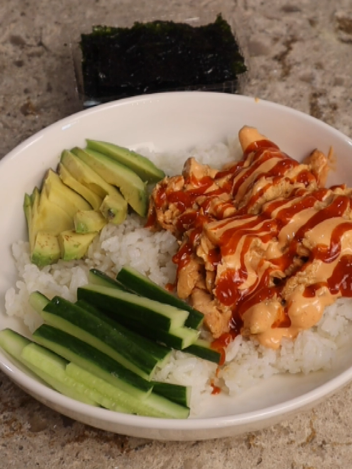Salmon Sushi Bowls  We rarely go out to eat, so here’s what I make at home when we want sushi for dinner. First I rinsed 2 cups of rice a few times, this is just regular long grain rice, not a sushi rice.  I add 2 cups of water and I cook that in my rice cooker on the white rice setting. I prepped a quick spicy mayo by just mixing mayo and sriracha together, again I’m just using regular mayo, not a japanese mayo, and I don’t measure, i just taste and adjust. I pat dry a salmon fillet with a paper towel.  To a bowl add 1 tablespoon of mayo, 2 tablespoons of soy sauce, 1 teaspoon grated ginger, and 1 teaspoon minced garlic.  Mix it all together and pour this over the salmon fillet and this went in my air fryer for at 400 degrees for 15 minutes. At this point the rice was done, so I dump it into a mixing bowl along with ¼ cup of mirin which is a seasoned rice vinegar, and using a rice paddle I gently folded the mirin into the rice which also cools the rice. Once my salmon was done I shredded it with a fork and I removed the skin and I let it cool slightly before I tossed it in my spicy mayo mixture.   To assemble my bowl I laid down a bed of the seasoned rice, along with some of the salmon, some sliced cucumber, sliced avocado, and I finished it with another drizzle of spicy mayo along with some additional sriracha.  And this gets served with seaweed sheets so that we can assemble bite sized portions of sushi at the table. Enjoy! #sushibowl #salmondinnerideas #sushiathome #easydinner #summerdinner #dinneridea #savemoney #dinnerathome