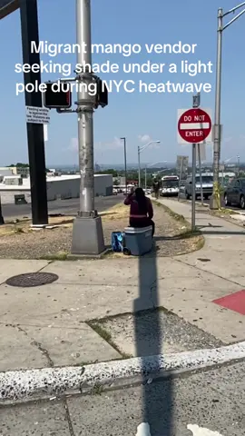 Migrant mango vendor seeking shade under a light pole in New Jersey during a heatwave a few miles outside the New York City area.