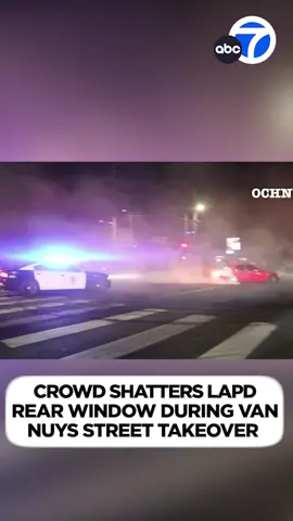 A mob surrounded an LAPD cruiser and broke a rear window after the officer tried to break up a street takeover in Van Nuys.