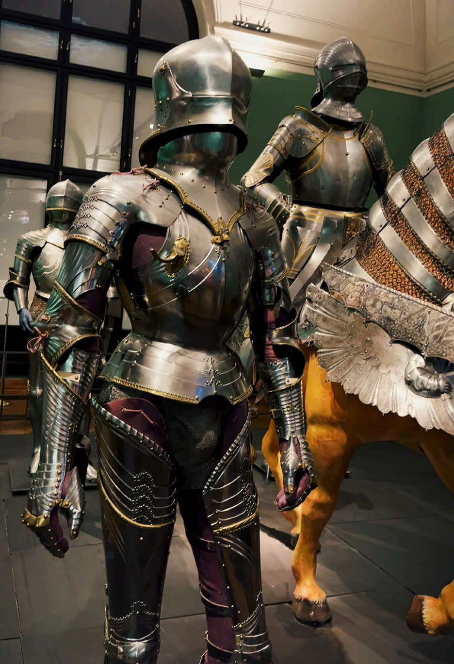 Gothic armour refers to a highly refined style of plate armor that originated in the Holy Roman Empire, particularly in the German-speaking regions, during the late 15th century. It is considered one of the most advanced and aesthetically pleasing forms of medieval armor, characterized by its elaborate craftsmanship and functional design. Key Features of Gothic Armour: 	1.	Fluting: 	•	The armor is often decorated with fluted ridges—narrow, raised lines that enhanced its strength and deflected blows. 	•	Fluting also reduced weight while maintaining rigidity, making the armor both strong and elegant. 	2.	Articulation and Mobility: 	•	Gothic armor was designed with articulated joints, allowing for greater movement in combat. 	•	Features like pauldrons (shoulder guards), cuisse (thigh guards), and gauntlets were meticulously crafted for flexibility without sacrificing protection. 	3.	Pointed and Sharp Aesthetic: 	•	Gothic armor is known for its sharp, angular designs, with pointed shapes in the sabaton (foot armor), gauntlets, and helmets. 	•	This aesthetic echoed the architectural style of Gothic cathedrals, emphasizing verticality and sharp angles. 	4.	Helmets: 	•	Typical helmets included the sallet (a rounded helmet with a long tail at the back) and the armet (a close-fitting helmet with a visor). 	•	These helmets often featured neck protection like the bevor or gorget. 	5.	Integration with Chainmail: 	•	Plate armor was complemented by chainmail in areas requiring extra flexibility, such as the armpits and groin. 	6.	Etching and Decoration: 	•	Gothic armor was often highly decorative, with etched designs, gilding, and engraved patterns that reflected the wealth and status of the wearer. Usage: 	•	Gothic armor was primarily used by knights and high-ranking soldiers during the late Middle Ages. 	•	It became prominent in tournaments as well as on the battlefield, offering superior protection against the increasingly powerful weapons of the time, such as crossbows and early firearms. Decline: By the early 16th century, Gothic armor evolved into the Maximilian style, which featured smoother surfaces and less fluting. Advances in firearms eventually rendered full plate armor obsolete on the battlefield, though it remained popular in ceremonial contexts. #travel #sightseeing #history #dji #osmomobile6 #europe #armor #armour #vienna #wien #gothicarmor #austria #österreich🇦🇹 