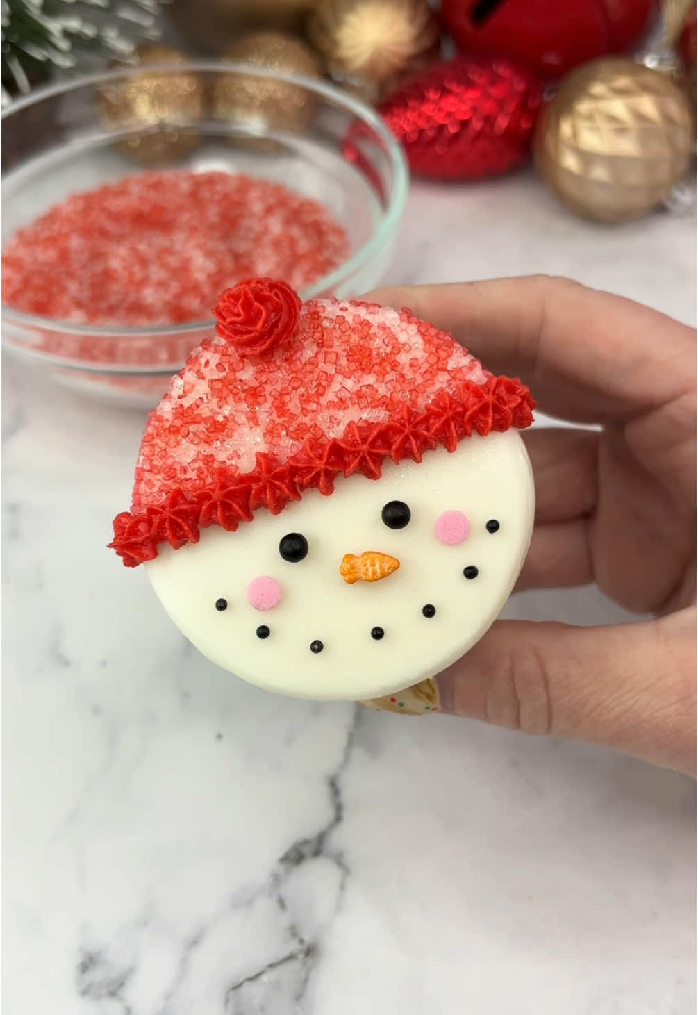 Frosty ☃️❤️🧁 24 days of Christmas treats 🎅🏼🧁🍪 ☃️ Start with a flat top on your cupcake.  ☃️ Add a strip of parchment paper, leaving 1/3 uncovered.  ☃️ Gently press it into sanding sugar or sprinkles.  ☃️ Peel off the parchment paper.  ☃️ Use piping tip 18 to pipe a coloured border and a bobble.  ☃️ Add sprinkles for the face. If you can’t find a carrot 🥕 sprinkle the. A normal orange one looks great too ☃️❤️ Enjoy ☺️❤️🎄 #cupcake #christmasbaking #snowman #cakeart #bakinginspo #cakedbyrach #christmastreats #christmascountdown #christmastreats 