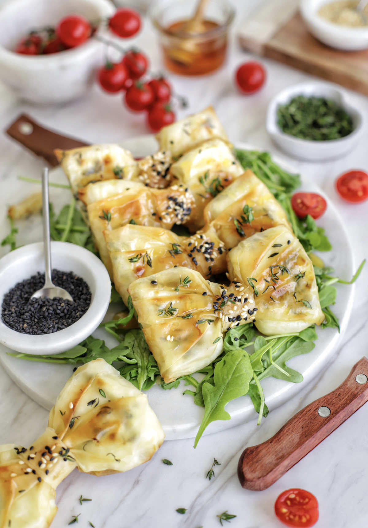 Bow-shaped 🎀Feta Phyllo Pastry  Method  • 200g feta cheese • 2 sheets of phyllo pastry • Fresh thyme leaves • 2 tablespoons honey • 1 tablespoon black and white sesame seeds Melted butter for brushing Instructions: 1. Preheat your oven to 160°C and line a baking sheet with parchment paper. 2. Place one sheet of phyllo pastry on a clean work surface and brush it with melted butter. Sprinkle fresh thyme leaves over the surface. Layer the second sheet of phyllo pastry on top. 3. Gently squeeze the layered phyllo pastry in the middle, creating a bow shape. 4. Place a piece of feta cheese on each side of the squeezed center. 5. Fold the right and left sides of the phyllo pastry inward, forming the bow shape and encasing the feta cheese. 6. Cut a 1-inch line in the center of one strip of phyllo pastry without cutting all the way through. Place it on top of the bow-shaped pastries to complete the bow look. 7. Brush the tops of the pastries with melted butter for a golden, crispy finish. 8. Sprinkle black and white sesame seeds over the center strip. 9. Bake in the preheated oven for 30 minutes. 10. Drizzle the pastries with honey. 11. Serve the baked feta phyllo pastries warm as a delightful appetizer or snack.