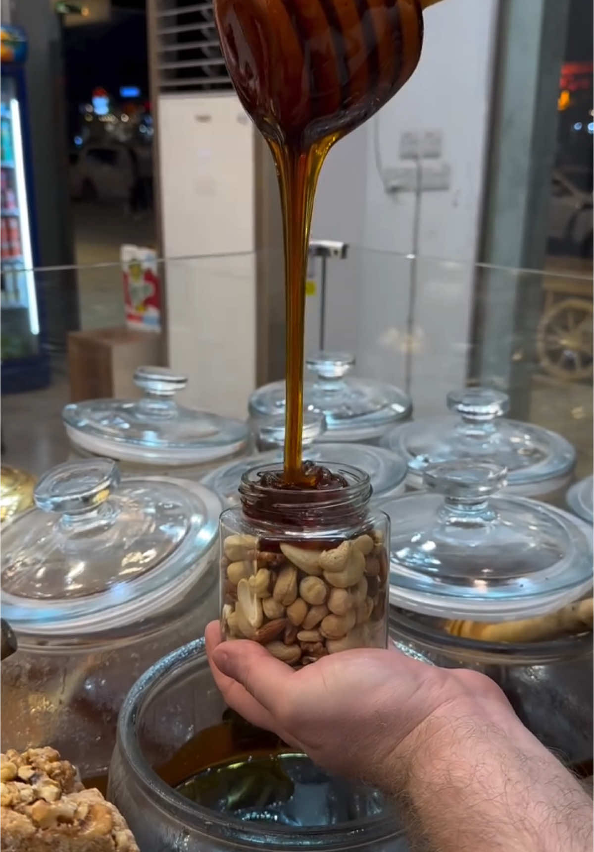 Honey and nuts at Kajo Baghdad shop, Iraq 🇮🇶  In Iraq, the combination of honey and mixed nuts—such as cashews, almonds, and pistachios—is a traditional treat cherished for its health benefits and rich flavor. This blend is not only enjoyed as a snack but also serves as a popular topping for yogurt and sweets, and is often paired with bread for a satisfying meal. Iraqi honey, sourced from diverse floral regions, adds unique flavors to this mix, with varieties from wildflowers, citrus, and acacia trees being particularly prized. A jar of honey with nuts is also a meaningful gift in Iraqi culture, symbolizing health, prosperity, and a sweet life.
