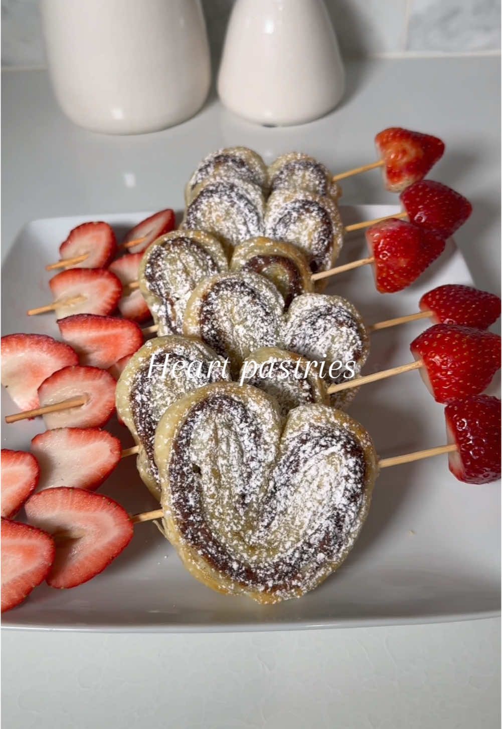 Pastry Hearts ♥️🤍 Lay out thawed puff pastry sheet Spread whatever filling you'd like, I used Nutella  Lay another sheet of pastry  Cut and shape into hearts Top with egg wash  Bake at 400 degrees for 15 minutes Top with powdered sugar Tip: Soak your skewers in water before so they don’t burn #pastry #valentine #galentinesday 