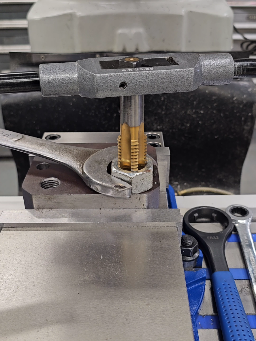 Old School Machinist Trick For those wondering.  It can be difficult to start a tap perpendicular to the workpiece without some sort of guide.  Threading the nut onto the tap allows progressive advancement.  As the tap goes deeper, the nut follows and provides a surface to help keep the tap from wandering.  The tap in this video was 1.00