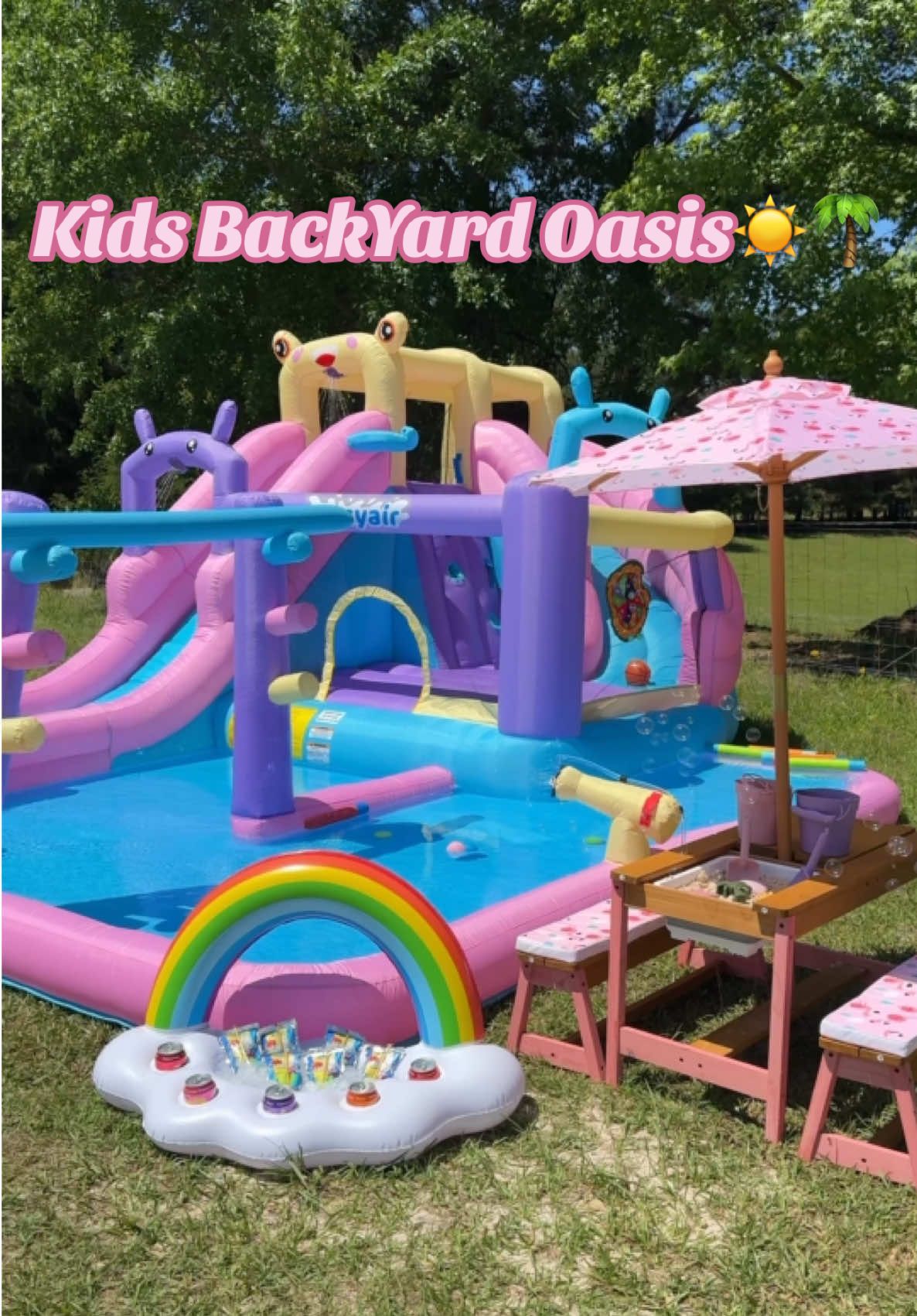 Let’s set up a kids backyard oasis!! ☀️🌴 I started with this blow up water slide / bounce house inflatable! It comes with little games too! Limbo, a Velcro ball game , and basketball! Then we added the most adorable little picnic table! It has cushion seats and a cute little umbrella. It also comes with little cubbies for an activity center. We filled ours with sand and sand toys!!☀️☀️ Then I added some water blasters and reusable water balloons! The reasonable water balloons are so cool. The outer liner is magnetic so it seals the water inside and you can use them over and over again!! Then we added the cutest rainbow cooler and I filled it with their favorite drinks! They love Capri Suns and Poppis. Then for fun effect we added a bubble machine!!💕 Now we are ready for long summer days.☀️☀️ They have been playing on this every single day since setting it up.❤️❤️😍 #outdoorliving #backyardvibes #poolideas #summerparty #outdoorentertaining #summervibes #summerparty #poolparty #kidsactivities #kidstoys #outdoorplay #kidsessentials #outdooractivitiesforkids #toddlermusthaves #summertoys 