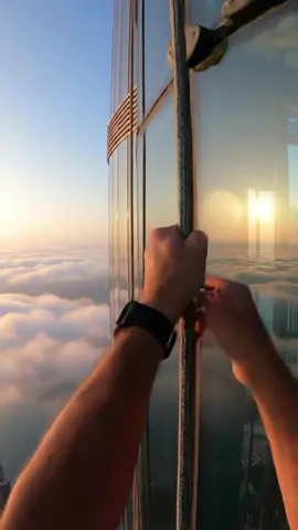 Burj Khalifa, Dubai POV of hands gripping smooth glass and steel as a climber ascends the Burj Khalifa at sunrise, clouds drifting beneath, golden light glinting off the building’s edge.