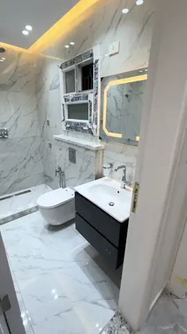 “حمّام آخر شياكة، معمول على طراز مودرن يخطف العين! كله سيراميك رخام أبيض في رمادي، يلمع من النظافة كأنك داخل فندق ٥ نجوم. السقف فيه إضاءة سبوتات نازلة كده تنور المكان زي النهار، ومعاها كمان إضاءة مخفية صفرا من فوق مديّة جو دافي وحلو. الدُش نازل من السقف على شكل شمسية، يعني دش ملوكي يغرقك وانت واقف مرتاح. التصريف معمول تحت في الأرض بشكل رايق من غير ما تشوف مواسير ولا صرف طالع. القاعدة المعلّقة شكلها نضيف ومودرن، والحيطة وراها مبنية ومغطيّة الخزان، يعني مفيش أي حاجة باينة تشوه المنظر. جنبها شطاف صغير، عملي وسهل الاستخدام. وفيه وحدة حوض شيك، لونها غامق وعليها حوض ابيض، ومعاها مراية كبيرة #سباكة #bathroom #bathroomdesign #decor #بروسلين #حمامات #حمامات_مودرن #plumber #egypt #الامارات #مهندس_ديكور #سراميك #مصر #افكار #ابداع #تصميم #ديكور #ديكورات_داخليه 