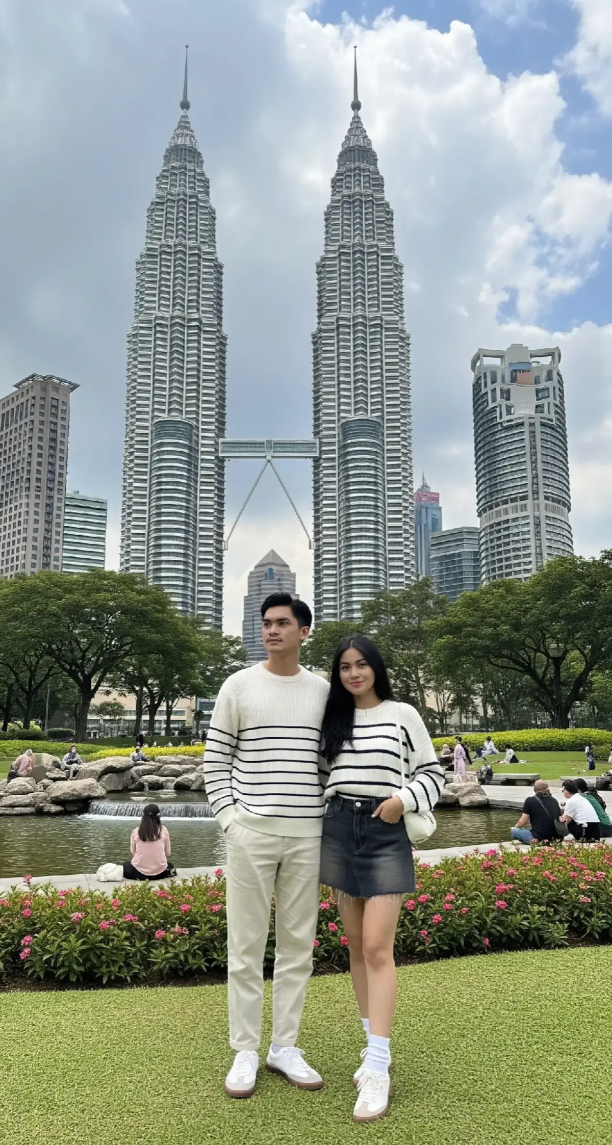 Promt Gemini:A very realistic styled photo on a bright sunny day taken with an old Nokia Android camera, showing a dramatic view of the Petronas Twin Towers in Kuala Lumpur, Malaysia. The pale blue sky with thick clouds creates a dramatic atmosphere that contrasts with the futuristic architecture of the two identical towers towering and connected by a skybridge in the middle. In the foreground is a green and beautiful city park. You can see well-maintained green grass, flowering bushes, a small clear waterfall, several shady trees, and several people who seem to be relaxing. The natural nuances combine with modern urban elements, creating a calming visual harmony. The main subjects are a young Sundanese couple: the man is wearing a white horizontal striped knit sweater, loose-fit ivory white trousers, and white sneakers with light brown soles. the woman is wearing an oversized striped knit sweater to match the man's, a faded black denim mini skirt with a raw hem, white ankle socks, white sneakers similar to the man's, and a small white bag. Technical details: Photo style: very realistic and natural Aspect ratio: 3:4 (portrait orientation) Color tone: natural, balanced contrast, not oversaturated @Ariel Tatum  #gemini #chatgpt #faceswap #ai #klingai #googlegemini #promt #arieltatum #fypシ #aiphotography #trendddddddddddddddd #trendingggggggggggggggggggggggggggggggg #fypppppppooppppppppp #xycbaa #foryou #xycbaaaaaaaaaaaaaaaaaaaaaaaaaaaa #xyczba #trending #aiphoto #trending?song🔥 #malaysia #petronas 