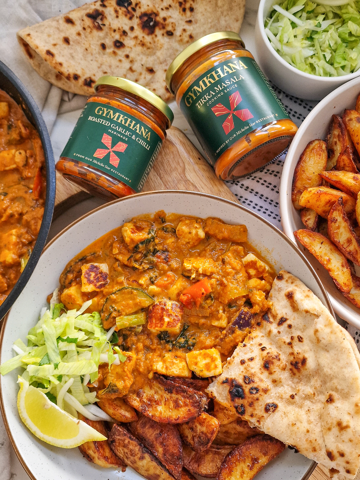 Halloumi & Vegetable Tikka Masala with Garlic & Chilli Potato Wedges AD / On a night when all you want is a lovely, lazy Indian takeaway, you have got to try this really simple, insanely delicious Veggie Tikka Masala and spiced wedges. You don't have to faff around with loads of ingredients and spend hours cooking, because @Gymkhana Fine Foods  have done all of the hard graft for you! Their sauces and marinades are 100% natural. There's no preservatives and absolutely no artificial colours. They're inspired by the 2 Michelin Star Mayfair restaurant, Gymkhana. You don't have to trek over to Mayfair to get them as these have just landed in Sainsbury's stores - I've written up the recipe for this below, let me know if it's going on your shopping list! A x #summercurry  #gymkhana  #easywin  Feeds 4 1kg Maris Piper potatoes Vegetable oil 2 tbsp Gymkhana Roasted Garlic & Chilli Marinade 225g block of halloumi cut into 1cm cubes 260g tub of mixed mediterranean vegetables 300ml Gymkhana Tikka Masala Sauce Peel the potatoes, cut them into wedges and soak them in cold water for a couple of minutes, changing the water twice to rinse off the starch. Place the wedges in a saucepan and cover them in cold salted water. Bring the potato water to a simmer and cook for around 5-7 minutes. The potatoes should still be firm enough to shake them up without them breaking. Heat the oven to 220C fan Drain the potatoes in a colander and give them a good shake. Allow them to steam dry. Tip the wedges into a pan and brush with vegetable oil and season generously with salt. Roast in the oven for around 20 minutes or until nearly cooked. Drizzle 2 tbsp of the chilli marinade over the top. Use a fish slice to turn them over until coated. Return to the oven for around 5 more minutes, or until cooked. In the meantime place the halloumi in a dry, hot pan and fry for 5 minutes, turning regularly until golden brown. Set the halloumi aside and add a drizzle of oil to the pan. Add the vegetables and fry for 5 minutes until soft. Stir in the Tikka Masala sauce and a couple of tablespoons of water. Return the halloumi to the pan and give it a good stir. Simmer for 3-5 minutes until heated through. Serve with the chilli wedges, some shredded lettuce and naan if you like. #comfortfood #cosydinner #delicious #sotasty 