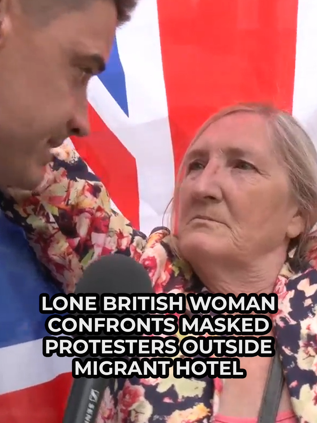 Ben Leo speaks to a woman who is defiantly standing in front of masked protesters outside a migrant hotel in London. The woman, holding the Union Jack, said she feared for her children and grandchildren as she stood alone infront of a sea of protesters. GB News host Ben Leo said: 'That woman there, brave, courageous, and dare I say it speaks for probably a lot of the country right now.' #MigrantHotel #MigrantCrisis #London #BenLeo #GBNews
