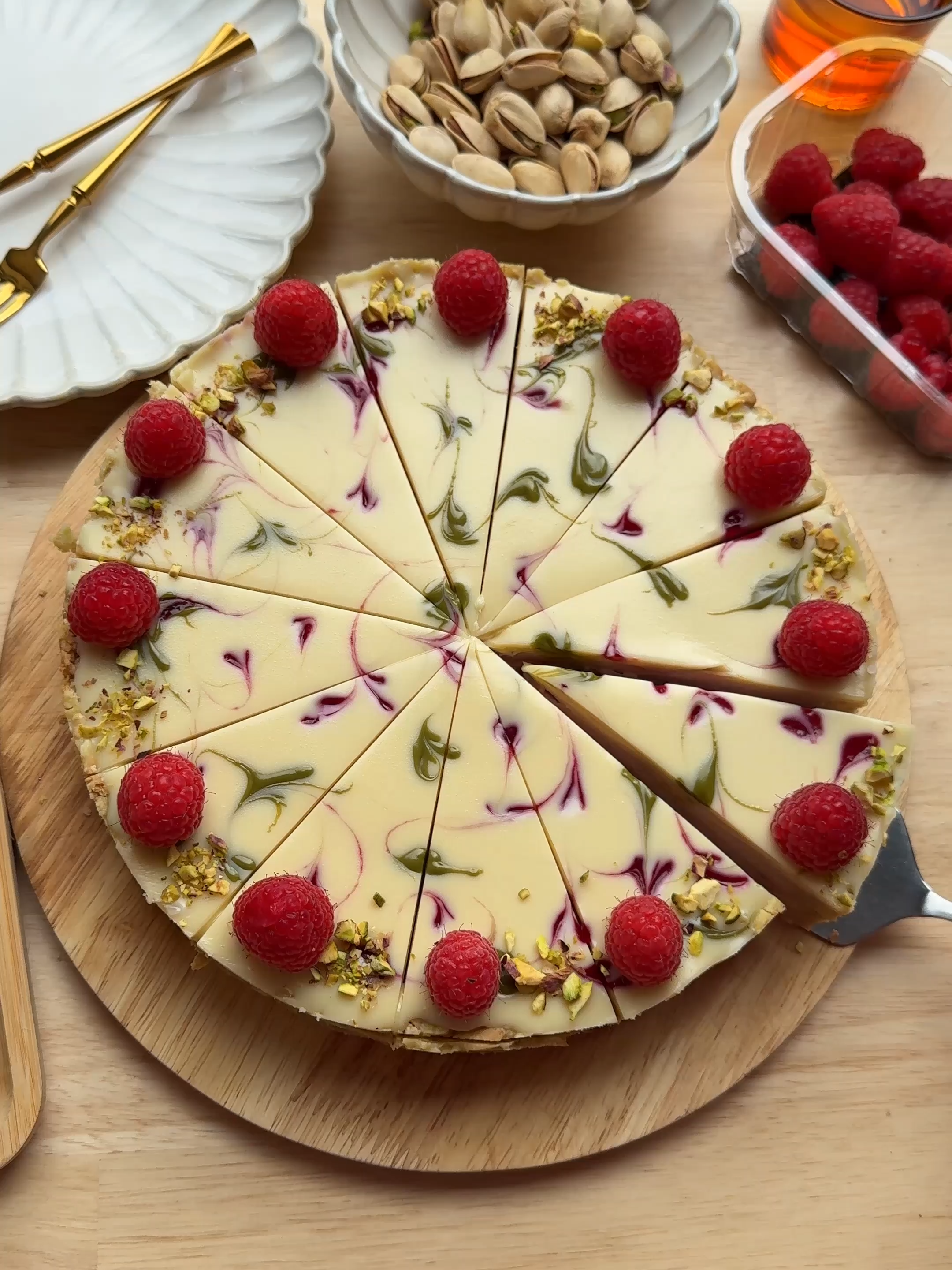 RASPBERRY PISTACHIO CHEESECAKE #pistachio #food #recipe #cheesecake #raspberry #fy #fyp #foryoupage COOKIE BASE 50 ml heavy cream 150 g white chocolate 140 g petit beurre cookies (or tea biscuits) 35 g pistachio paste RASPBERRY MIXTURE 200 g raspberries (frozen) 75 g granulated sugar CREAM 250 g mascarpone 50 g raspberry mixture 8 g whipping cream stabilizer (klopfix) 35 g powdered sugar 8 g vanilla sugar (1 packet) 250 ml heavy cream FILLING 90 g pistachio paste 35 g raspberry mixture TOPPING 100 g white chocolate 40 ml heavy cream  raspberry syrup pistachio paste GARNISH pistachios (unsalted) raspberries INSTRUCTIONS Heat the cream (50 ml) almost to a boil. Add the white chocolate (150 g), let it sit for 1 minute, then stir until smooth. Crush the cookies and place them in a bowl. Add the chocolate ganache and pistachio paste, then mix well. Line a springform pan with parchment paper and spread the cookie mixture evenly over the bottom. Press down lightly with the back of a spoon, also pressing it up the sides to form a rim. Place the raspberries together with the sugar in a frying pan over medium heat. Bring to a boil for 5–7 minutes, stirring occasionally. Strain the raspberry mixture through a sieve into a bowl to remove the seeds. Press well with a spatula or spoon. Put the raspberry syrup into a piping bag and set aside. In a bowl, combine mascarpone, raspberry syrup (50 g), stabilizer, powdered sugar, and vanilla sugar. Mix for 1 minute. Gradually add the heavy cream (250 ml) and whip until firm. Spread the pistachio paste (90 g) over the cookie base. Cover with half of the cream and smooth the surface. Pipe lines of raspberry syrup (35 g) over it. Cover with the remaining cream and smooth again. Heat the cream (40 ml) almost to a boil. Add the white chocolate (100 g), let it sit for 1 minute, then stir until smooth. Pour the ganache over the cream layer. Pipe small dots of raspberry syrup and pistachio paste on top and use a toothpick to create a pattern. Cover the cheesecake and let it set in the refrigerator for at least 6 hours, preferably overnight. Cut into slices and garnish with fresh raspberries and chopped pistachios.