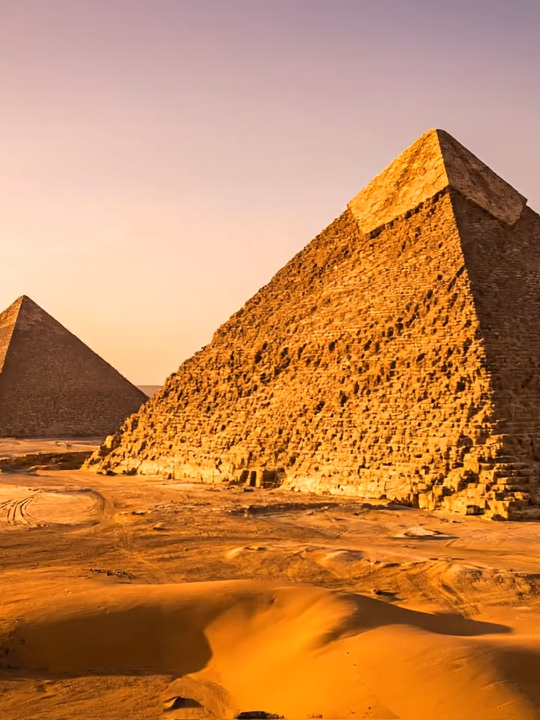 Majestic Pyramids Cinematic Sunset View Our #ThrowbackThursday takes us to the awe-inspiring Pyramids of Giza in Egypt, one of the Seven Wonders of the Ancient World. Built as tombs for pharaohs, these colossal structures are a testament to ancient Egyptian engineering and belief. Our drone flyover aims to convey their enduring grandeur as the desert sun sets.  #AI #Pyramids #Egypt #AncientWonders #VirtualVoyager