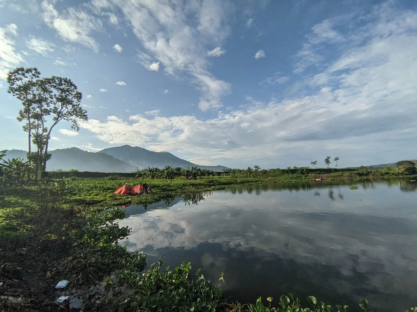 Pagi yang cerah di pinggir danau. Langit biru berhias awan, gunung menjulang, dan dua tenda kecil jadi saksi bisu keindahan alam ini. Bener-bener tempat yang pas buat rehat sejenak dan isi ulang energi. Siapa yang kangen liburan kayak gini? 🏕️✨  Lokasi : Waduk Selorejo Ngantang Malang #mancing #ngantang #fyp #naturelovers #camping 