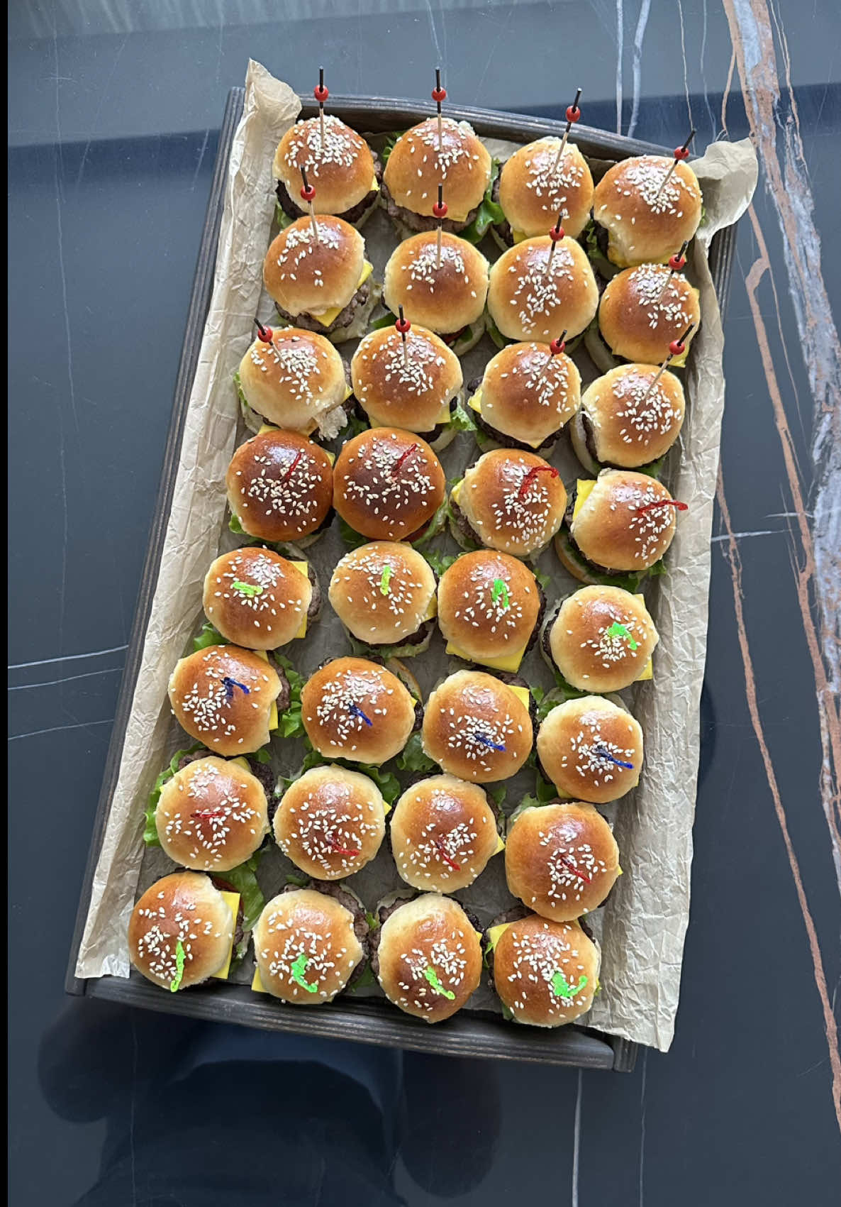 Прекрасная закуска на два укуса. Понравится и детям, и взрослым. Мини Бургеры 🍔  Ингредиенты: Для теста: Пшеничная мука 400 г Молоко 180 мл Дрожжи сухие 11 г Куриное яйцо 1 шт Сахар 2 ч.л Соль 1 ч.л Сливочное масло 30 г Дополнительно: Кунжут по вкусу  Яичный желток + 2-3 ст.л сливки для смазывания  для котлеток: Фарш мясной 1 кг Соль, перец по вкусу  Для начинки: Помидоры 200 г  Огурцы корнишоны маринованные 200 г Листья салата  Сыр плавленый  Майонез 80 г Кетчуп 40 г Горчица по вкусу В кружке с теплым молоком растворить дрожжи.  Просеять муку в глубокую миску, добавить соль и сахар. Добавить к муке тёплое молоко, яйцо и масло, вымешать лопаткой, выложить тесто на рабочую поверхность и далее продолжать вымешивать руками.  Сформировать шар и вернуть в миску. Накрыть пищевой пленкой и дать подняться около часа в теплом месте. Тесто должно увеличиться в объеме в 2 раза. Поднявшееся тесто аккуратно выложить на немного припыленную мукой рабочую поверхность, разделить на равных части и сформировать из них шары.  Переложить швом вниз на выстеленный пергаментом противень, накрыть чистым полотенцем и дать подойти в теплом месте, пока они не увеличатся в размере в полтора-два раза, около 40–60 минут. Расстоявишиеся булочки можно смазать желтком и посыпать кунжутом. Выпекать при 200°С около 15–17 минут до готовности и темно-золотистого оттенка. Дать готовым булочкам остыть перед тем как разрезать. Приправьте фарш солью и черным перцем. Хорошо вымешайте и отбейте фарш. Разделите на одинаковых шариков. Каждый мясной шарик расплющите в плоскую котлетку толщиной 7-8 мм и диаметром на 2 см больше, чем диаметр булочек. Обжарьте котлетки в небольшом количестве растительного масла с обеих сторон - по 2-2,5 минуты с каждой стороны. Переложите их на тарелку и накройте каждую квадратиком плавленого сыра. Соберите бургеры. Каждую булочку разрежьте пополам. Нижнюю половинку смажьте соусом из майонеза и кетчупа. Положите на нее кусочек салата — можно свернуть его в два-три раза. На салат - ломтик помидора, затем котлетку с сыром. Смажьте срез верхней половинки булочки соусом, положите на нее пару ломтиков маринованного огурца и водрузите ее на нижнюю конструкцию. Скрепите бургеры специальными шпажками. Приятного аппетита