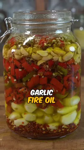 The best homemade garlic fire oil I have ever tried, using fresh chillies from your garden and turn the leftover solids into a delicious paste or condiment🌶️ Ingredients: * 1 litre avocado oil (or neutral oil: sunflower, rapeseed, grapeseed) * ~25 garlic cloves (200 g), peeled * 15 fresh chilies (mixed red & green), roasted 40 minutes at 180°C, then sliced * ½ cup chili flakes (about 30 g) * 1 cup (140 g) roasted peanuts, unsalted Step by step: Sterilise a glass jar and make sure it’s completely dry and slightly warm. Layer the ingredients in the jar: chili flakes at the bottom, then garlic cloves, then the sliced roasted chilies, and finally the roasted peanuts on top. Heat the oil in a saucepan to about 160–170°C, hot but not smoking. Carefully pour the hot oil over the layered ingredients in the jar until everything is fully submerged. Stir gently with a clean spoon to release any trapped air bubbles. Leave to cool completely at room temperature. Once cooled, stir again and strain through a fine sieve or cheesecloth into sterilised glass bottles. Store in the fridge and use within 4–6 weeks. With the strained solids (garlic, chilies, peanuts, flakes), blend into a smooth paste, adding a spoonful of oil if needed. Spread the paste thinly on a dehydrator sheet and dry at 60°C for 6–8 hours, or on parchment in the oven at 70–90°C for 3–5 hours with the door slightly ajar, until crisp. Break into chunks, grind into a fine powder, and store in an airtight jar. #spicy #garlic #chillies #asmr #fyp 