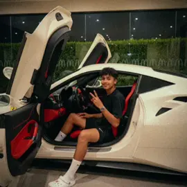 Prompt: A young man sitting confidently inside a sleek, white luxury supercar with butterfly doors open at night. The car interior is a striking red and black with racing seats and a modern dashboard featuring a digital display and Ferrari logo on the steering wheel e man is wearing a black t-shirt, black shorts.#car #ai #chatgpt 