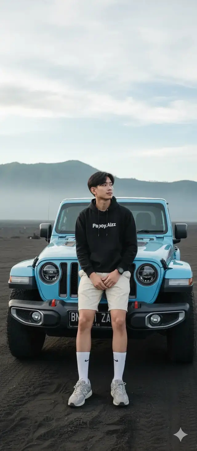 Pormpt : Buatkan Foto vertikal dengan kualitas tinggi, ultra realistis dan tajam (resolusi HD), menampilkan seorang pria yang ada di foto (jangan ubah wajah),gaya rambut komma hitam rapi menutupi dahi sedikit acak-acakwn, dengan kulit cerah duduk santai di atas kap depan mobil STORM-46, Jeep Wrangler JL Rubicon 2 Door 2020 warna biru muda, dengan plat nomor BN 21 ZA berwarna hitam dan tulisan putih yang terlihat jelas di bagian depan mobil. Lokasi berada di hamparan pasir hitam luas khas Gunung Bromo, dengan latar belakang pegunungan hijau berkabut dan langit cerah berawan. Pria tersebut mengenakan hoodie hitam bertuliskan Papoy.Aizz, celana pendek crem, kaos kaki putih panjang dengan logo Nike, dan sneakers abu-abu New Balance. serta Apple Watch warna hitam di tangan kiri. Tangan diletakkan santai di lutut, tubuh tegap, menatap ke arah kanan atas dengan ekspresi wajah tenang dan percaya diri. Pose terlihat natural dan kasual, dengan pencahayaan alami pagi hari yang lembut. Gaya fotografi menggunakan kamera profesional full-frame, dengan lensa prime 85mm f/1.4, menghasilkan efek bokeh halus di latar belakang dan fokus sangat tajam pada subjek utama. Komposisi simetris, framing rapi, dan tone warna natural memberi kesan hasil foto profesional seperti majalah outdoor lifestyle. #aitrending #aiphoto #pyfツ #gemini #soundviral 