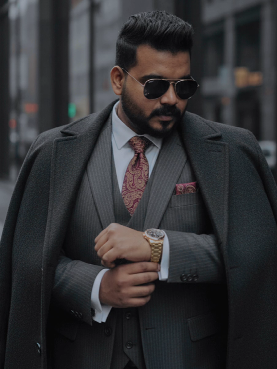 #Ai #googlegemini #chatgpt #trending #prompt  (PROMPT) With the man in the photo uploaded create a professional, cinematic realistic fashion photograph of a dapper and confident young man in last 27s with black hair and black beard. He is wearing reflective sunglasses and is dressed in a sharp, dark, pinstripe three-piece suit, complemented by a crisp white shirt and a patterned tie, golden watch. A heavy, dark wool overcoat is elegantly draped over his shoulders. The man is captured in a candid, sophisticated pose, looking down as he adjusts his shirt cuff. The setting is a modern urban environment, with the subject standing before a sleek building with large, dark, reflective glass windows. The lighting is moody and natural, creating soft, dramatic shadows and highlighting the textures of the fabric. The overall aesthetic is cinematic, high-end, and powerful. Style: Men's fashion editorial, photorealistic, hyper-detailed, sharp focus, cinematic color grading, 8K resolution, hyperrealistic, FHD, Sony Lens.