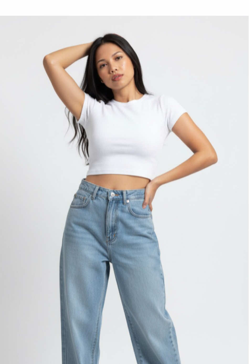 Prompt: Use this image to cReate Hyperrealistic editorial photograph Wear a simple white crop top that reveals, combined with high-waisted feminine jeans, wide and baggy pants, along with white. Her pose is standing, with one hand raised touching the hair and the other resting on the hip, transmitting confidence and freshness. Flat white studio minimalist background that highlights her silhouette. Urban fashion editorial style, soft and diffuse lighting, highlighting clothing textures and face features. Realistic 4KHD photography, ultra detailed, magazine quality. ed parameters: --ar 2:3 --v 6 --q 2 --style raw --hd --c 25 --s 750 #trending #gemini #prompt #fyp #geminiai 