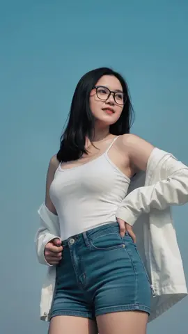 Seorang gadis Indonesia muda cantik sexy berkulit cerah duduk santai di luar ruangan. Ia mengenakan tank top putih ketat, denim shorts biru, parka putih terbuka melorot di bahu, dan kacamata. Rambut lurus seleher tertiup angin. Kamera high angle dari atas menyorot ke bawah, menangkap momen saat ia tersenyum ceria sambil menata rambut. Latar belakang biru laut dan langit cerah menambah nuansa fresh dan youthful. #gemini #jasaeditfoto #ai #foryoupage #trendgeminiai 