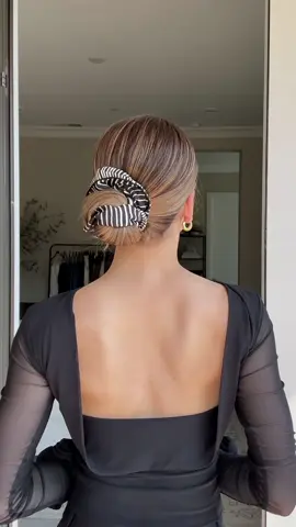 A chic scrunchie bun you need to try! Start by gathering your hair into a ponytail. Place your hand on top and tilt your head forward slightly. Flip the ponytail over your thumb so it rests neatly on top of your head. This little tilt makes all the difference! Slip a silk scrunchie over the base to form a mini bun, then give the scrunchie one twist. As you bring your head upright, switch hands and pull the ponytail to the side of the bun, tucking it behind the fabric. Wrap the scrunchie around everything, securing the ends inside for a soft, effortless look 💁‍♀️ #hair #hairtutorial #updo #hairstyle 