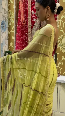 a beautiful saree perfect for a special occasion. The woman wears a light yellow, almost lime-colored saree with subtle, shimmering stripes in a darker, brownish hue. The fabric has a sheer, flowy quality, and the border is delicately embellished with sequins that catch the light. She's paired it with a sparkly gold blouse, and the look is completed with elegant gold earrings. The overall style is sophisticated and perfect for an evening event. #sareelove #indianfashion #ethnicwear #sareestyle #partysaree    