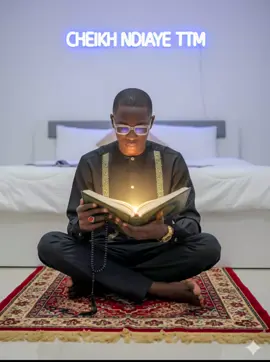 #gmini #cheikhndiaye0335 👇👇 Crée une image ultra réaliste en 8K de la personne sur la photo assise sur un tapis de prière dans une chambre paisible et moderne, éclairée dans des tons blancs et doux. Elle tient dans ses mains un grand livre coranique ouvert, baigné d'une lumière chaleureuse venant de la page. Dans son autre main baissé, un chapelet long (sebha) glisse doucement entre ses doigts. Derrière elle, le mur affiche une enseigne lumineuse cheikh ndiaye ttm en néon bleu vif, projetant une lueur douce sur le décor. Le lit en arrière-plan est proprement fait, avec une couverture blanche et des coussins discrets, renforçant l'ambiance calme et spirituelle de la scène. L'expression de la personne est sereine, concentrée, paisible. L'atmosphère dégage une sensation de connexion intérieure, de foi profonde et de gratitude. La lumière met en valeur les plis du tissu, la texture du tapis de prière, et les détails fins du livre sacré. Style: hyperréaliste, éclairage cinématographique, textures complexes, ambiance spirituelle et moderne. Scène centrée sur la paix intérieure, la méditation et la lumière de la foi.