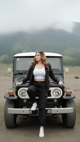 prompt gemini ai liburan di bromo : Edit foto ini dengan gaya casual modern, duduk di atas kap depan Jeep Toyota Land Cruiser klasik warna hitam, terparkir di padang pasir kawasan Gunung Bromo. Latar belakang menunjukkan perbukitan hijau khas Bromo yang tertutup kabut tebal, menciptakan suasana sejuk dan alami. Disamping jeep terlihat sedikit sisi jeep lain berwarna putih. Sedang duduk di tengah kap Jeep dengan posisi Satu tangan berada di kap mobil dan satu tangan lagi diatas paha, posisi kaki menyilang santai. la memakai kaos croptop warna putih dan jaket parka hitam terbuka, celana panjang kargo hitam, dan sepatu kets converse putih. Pose santai menatap ke samping. Kamera menggunakan low angle sinematik untuk menonjolkan suasana dramatis dan pemandangan pegunungan. Pencahayaan alami mendung, tone warna hangat alami. Tanpa watermark, tanpa efek kartun atau lukisan. Buat semirip mungkin, jangan rubah wajahnya. Ukuran foto HD, rasio 9:16. #CapCut #geminiai 