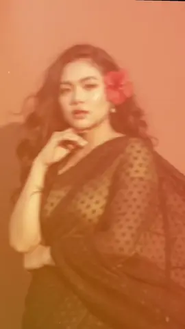 ✨: Create a retro vintage gainly but bright image of the reference picture but draped in a perfect black colour pinterest aesthetic retro saree. It must feel like a 90s move red baddie with a small flower tucked visibly into her curls and romenticising windly environment. The girl standing against a solid wall deep shadows and contrast drama, creating a mysterious and artistic atmosphere where the lighting is warm with a golden tones of evoking a sunset or golden hour glow and do not change original face.#gemini #indiadress 