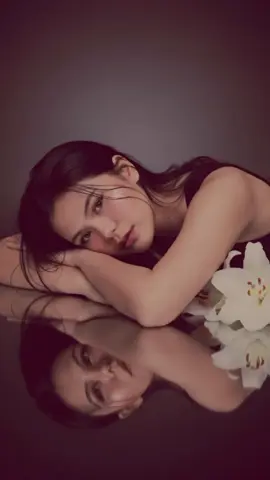 Gemini AI Prompt: A dreamy portrait of a beautiful woman lying gracefully beside white lilies, her head resting gently on her arms, is reflected perfectly on a glossy black surface. Soft cinematic lighting highlights her glowing skin and delicate facial features, with wet strands of hair framing her face. The mood is ethereal, romantic, and artistic, with a serene atmosphere, ultra-realistic, high-detail, professional studio photography, 8K. #gemini #fyp #fypシ #prompt 
