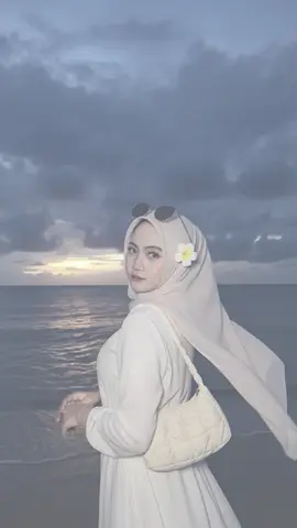 Promt GEMINI AI : Buatlah pemandangan pantai saat matahari terbenam yang sangat realistis dengan langit biru tua yang dramatis yang dipenuhi awan gelap, sedikit cahaya menerobos dekat cakrawala menghasilkan pantulan keemasan samar di air laut yang tenang. pantai tersebut remang-remang oleh sisa senja menciptakan suasana yang tenang dan muram, di latar depan berdiri seorang wanita Indonesia membelakangi kamera yang sangat cantik dengan kulit putih mulus dan bercahaya wajahnya disinari lembut oleh lampu kilat kamera menciptakan kontras yang indah dengan latar belakang yang gelap yang mengenakan jilbab cream panjang seperti tertiup angin yang dilengkapi oleh bunga kamboja plumeria putih segar yang diselipkan di belakang telinganya menambahkan sentuhan tropis dan feminim, lalu pakaiannya terdiri dari dress putih halus, pada kain putih lembut yang membangkitkan tampilan pantai yang segar tas bahu berwarna Gading berlapis dengan tekstur halus dan empuk bergantung santai di bahunya Iya melengkapinya dengan gelang emas halus di pergelangan tangannya dan cincin minimalis serta kacamata hitam diatas kepalanya sambil menaruh kedua tangan di depan dada dramatis yang tangan di depan dada yang santai dengan elegan menunjukkan rasa percaya diri dan ketenangan memadukan mode dan alam sangat sempurna gambar keseluruhannya memadukan tekstur yang sangat realistis pencahayaan alami dan pemandangan pantai yang atmosfer untuk menciptakan potret yang memikat dan damai secara visual jangan Ubah wajah #gemini #AI #Promt #Pantai #Fyp 