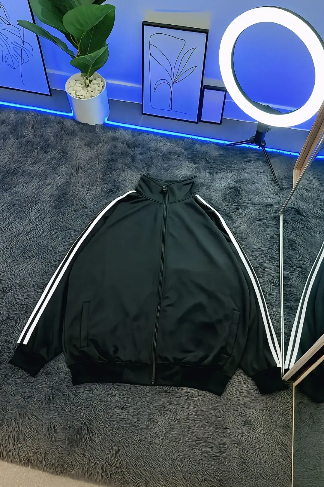 Prompt : Buatkan gambar produk ini jadi mirip asli diletakkan secara flat lay di atas karpet bulu berwarna abu-abu gelap. Latar belakang menampilkan dinding putih modern dengan lampu LED biru di bagian bawah, sebuah tanaman hias besar dalam pot putih berisi batu bulat putih, serta beberapa hiasan dinding bergaya minimalis yang disandarkan. Sebuah lampu ring light besar menyala terang dan mengarah ke jaket, memberikan pencahayaan yang merata. Terdapat cermin besar yang memantulkan jaket dan sebagian ruangan. Gaya foto diambil dari atas dengan rasio 9:16 dan resolusi 4K. Tampilan bersih dan bernuansa futuristik. #trendai #prompt #chatgpt #geminiai #affiliate 