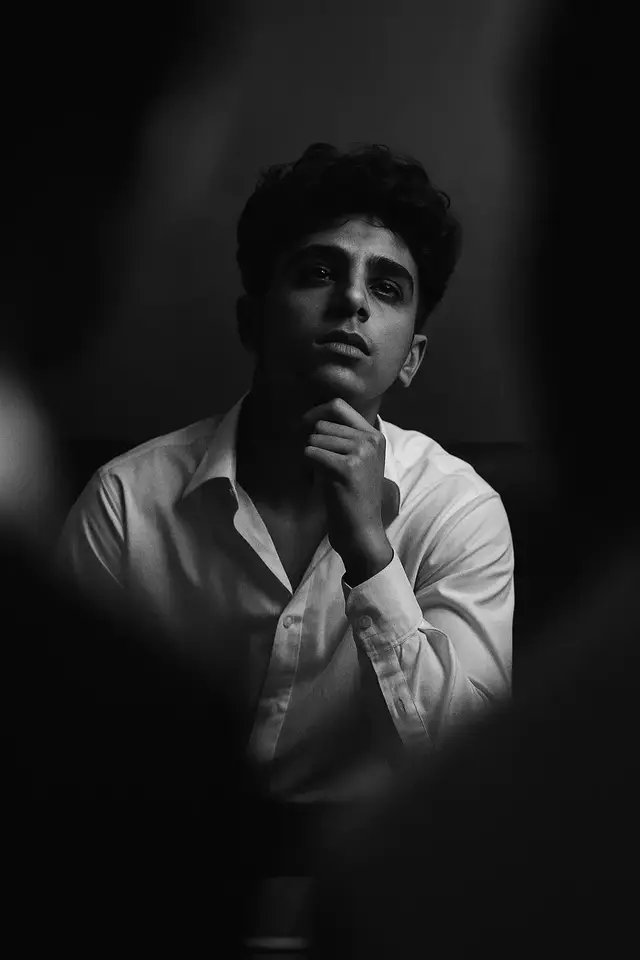 Convert this image into a fine black and white photography of a handsome young man ( take reference face as uploaded image face ) with dark , wavy hair ,his head tilted back in a moment of intense creative thought or ecstasy . He is wearing an open , loose white collared shirt , standing in a dimly lit study filled with stacks of books and papers . The image is captured with a slow shutter speed , creating dramatic horizontal motion blur that streaks the background and the edges of his for