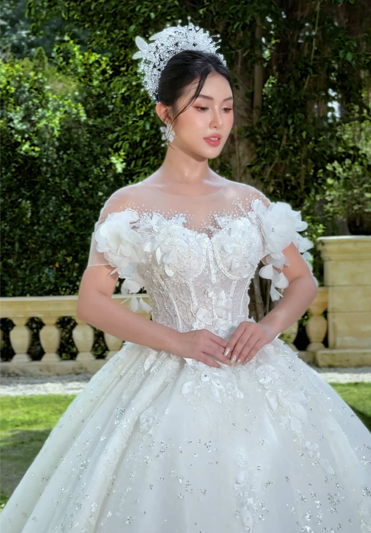 VÁY CƯỚI NEW Kiểu váy: Luxury dáng xòe to, mặc được tùng số 6 – 8 – 10  Tay áo: Trễ vai ngang Thiết kế: Đính đá bling pha lê nhuyễn nhỏ, bắt sáng tinh tế. Thân áo có form định hình chắc chắn, may mút độn ẩn tôn dáng vòng 1 Có dựng form gọng áo dẻo, đàn hồi, xiết eo tốt Tích hợp 12 gọng bên trong thân áo Đệm lót sau lưng, hỗ trợ ôm dáng • Voan: 4 lớp vải, hạn chế xuyên thấu • Áo: Mút ngực ẩn bên trong, dây thắt sau lưng độ hở 0,5cm mỗi bên Tùng váy: • 5 lớp dày dặn, có lớp lót mềm bên trong hổ trợ hạn chế xót ng/ứa • Phía trước ngắn, đuôi váy dài tạo độ sang trọng Chất liệu: Kim tuyến bling bling • Khóa váy: Phía sau đan dây ½ lưng áo, bên dưới có kéo zip (hỗ trợ nới vùng hông) • Trọng lượng váy: 3.100 kg #vaycuoidep #vaycuoiluxury #chuanbidamcuoi #dinhhon #LearnOnTikTok 