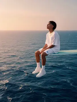 Recriei a capa do álbum “SOS”com IA da SZA Prompt usado: Recrie a cena da capa do álbum “sos” (Deluxe) da cantora SZA, em estilo fotográfico realista. Mostre uma pessoa sentada na ponta de uma prancha branca suspensa sobre o mar profundo, no meio do oceano com ondas azul-escuras e textura natural da água ao fundo. A pessoa deve estar com um camisa oversed branca e azul, shorts jersey branco, usando meias brancas até o tornozelo e tênis branco de cano alto e com corpo atlético. Ele deve estar sentado de perfil, com as pernas para fora da trampolim, olhando para cima de forma contemplativa, transmitindo serenidade e introspecção. A iluminação deve ser natural, com luz suave de fim de tarde, destacando os reflexos do sol nas ondas do oceano. O enquadramento deve mostrar bastante do mar, dando a sensação de imensidão com a pessoa distante. Substitua o rosto original pelo rosto do usuário, usando como referência a foto fornecida. Mantenha os traços do usuário de forma realista, integrando-os naturalmente ao corpo #IA #sza #imagem 