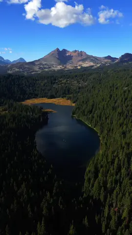 Soaring high above a stunning alpine lake in the Central Oregon Cascades, with its deep blue waters surrounded by dense forests, all leading the eye toward a magnificent volcanic peak on the horizon. The contrast of the still lake, endless evergreens, and rugged mountain landscape makes this view feel absolutely breathtaking—one of those scenes that captures the wild beauty of the Pacific Northwest 😍