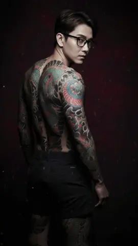 Hãy tạo giúp tôi bức ảnh mô tả một người quay lưng về phía máy quay, đầu hướng về phía ống kính, đeo kính. Nó phải trông giống như một bức ảnh ngẫu nhiên được chụp một cách tình cờ .Không làm biến dạng giữ nguyên chi tiết khuôn mặt 100% giống với hình tham chiếu. Hình ảnh nên trông giống như một bức ảnh chụp nhanh mà không có bất kỳ sự chú ý đặc biệt nào Phần lưng trần được che phủ hoàn toàn bằng hình xăm chi tiết theo phong cách Yakuza trải dài trên cả hai cánh tay, phần chân trong trang phục quần đùi ngắn , phần chân che phủ bằng hình xăm chi tiết theo phong cách yakuza trải dài trên hai chân . Ánh sáng studio ấn tượng với bầu không khí u ám, u ám. Bối cảnh mở ra nhiều cách diễn giải nghệ thuật.#cauut_gemini #art #photo #pomrt #vrial 