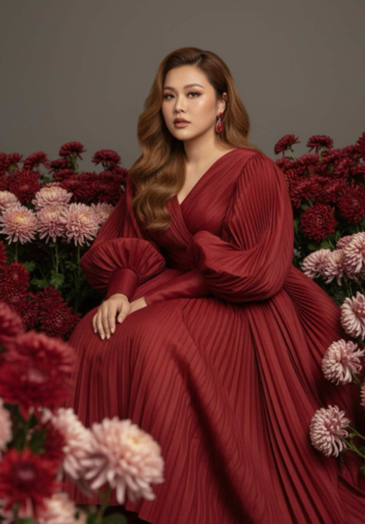 1. Open Gemini 2. Upload image  3. Paste the prompt Prompt : Use facial feature of photo attached.  An elegant high-fashion editorial portrait of a woman seated gracefully among lush clusters of chrysanthemums in shades of deep crimson, dusty rose, and soft blush. She wears a voluminous, pleated couture gown in rich crimson red, with oversized sculptural sleeves that echo the texture and form of the surrounding flowers. Her golden-brown long wavy hair frames her face naturally, and she gazes into the camera with quiet confidence and poise. Matching red earrings and embellished stilettos add to the bold yet refined styling. The composition blends fashion with floral artistry, creating a visual harmony between the organic softness of the blossoms and the structured folds of the fabric. The muted gray background enhances the drama of the red tones, giving the image a painterly, cinematic quality. Scale ratio: Model occupies ~70% of the frame height in a seated pose. Upper body and face make up ~35% of frame width, the focal point. Surrounding flowers cover ~60% of the frame, acting as both foreground and background. Visible leg and shoes emphasize ~15% of the lower frame, balancing elegance and strength. Camera settings: Lens: 50mm prime (classic portrait focal length, natural proportions) Aperture: f/2.8 (soft depth of field, sharp focus on subject, flowers gently blurred for layered depth) Shutter speed: 1/160s (to preserve sharpness while using controlled studio or diffused natural light) ISO: 200 (maintaining clean, warm tones and detail in shadows) Lighting: Soft, diffused light from the side, highlighting the gown’s texture and sculptural folds while creating gentle shadows on the face. Focus: Centered on the subject’s eyes, ensuring facial detail is crisp, while flowers and fabric fade into a painterly blur. Style tags: 8k ultra-detailed, luxury fashion editorial, couture photography, floral fine-art, cinematic tones, dramatic crimson palette, Vogue cover style, painterly elegance. #Gemini #ai #prompt #flowers #geminiai 