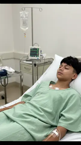 part1/prompt ⬇️ 👇  A young man lying in a hospital bed, wearing a green hospital gown, connected to IV drips and monitors, with medical equipment around the bed. His eyes are closed, looking weak as if he is resting after treatment. Realistic, clear face, no face change, ultra-realistic, HD, 4K hospital  environment.