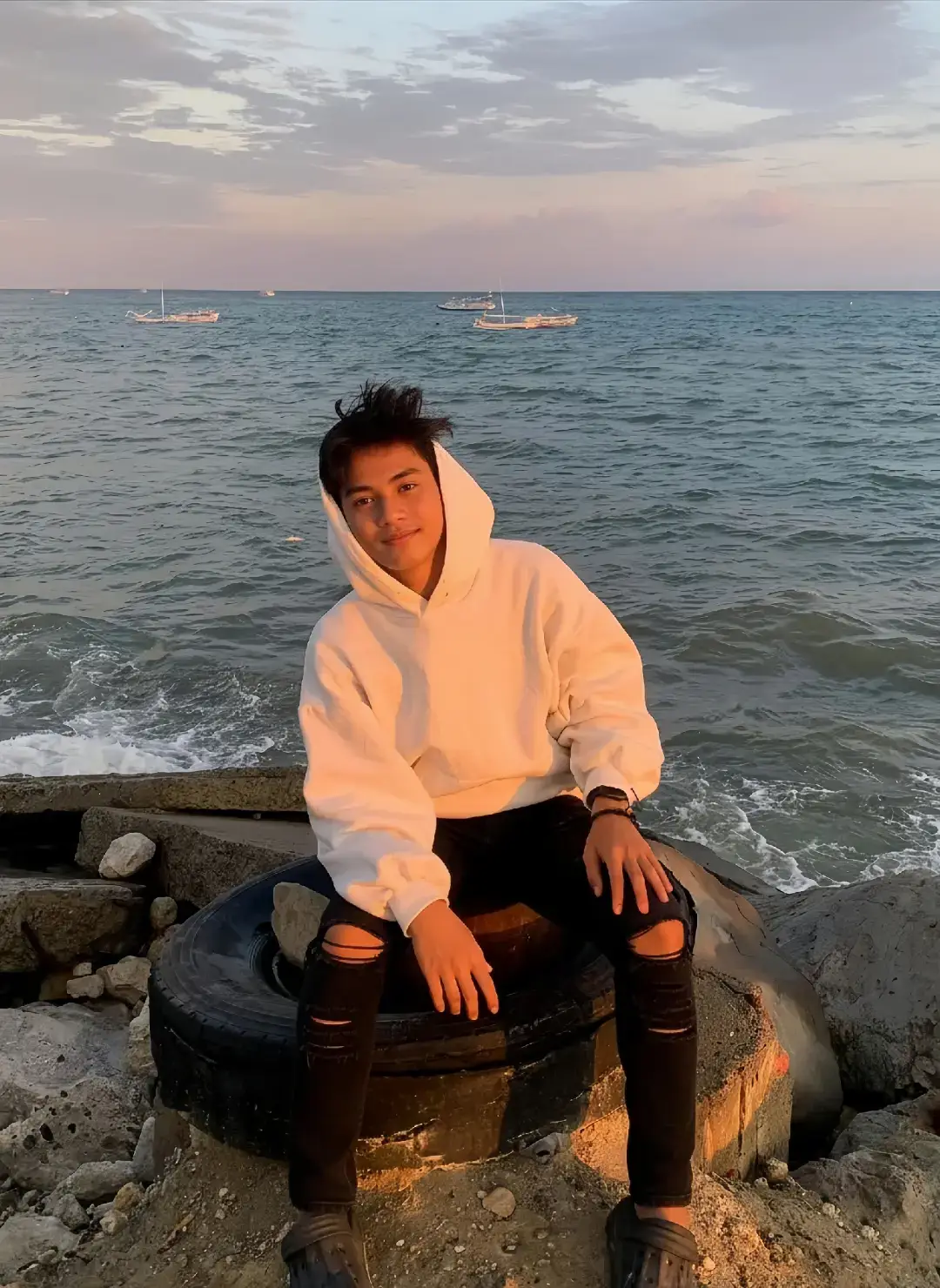 Cara Buat foto dipantai pake gemini ai Caranya? 1. Buka google/apk gemini di hp kalian 2. Masukan photo wajah kalian dan salin  prompt dibawah ini:👇🏻 Coba buat potret full-body seorang pria muda stylish di tepi laut saat senja (golden hour) dari subjek di atas. Subjek memiliki rambut hitam sedikit berantakan, mengenakan hoodie berwarna putih kebesaran, celana jeans hitam robek, dan sepatu sandal berwarna gelap. Terdapat jam tangan dan gelang di pergelangan tangannya. Dia duduk santai di atas ban bekas besar yang terletak di antara bebatuan di pinggir pantai, dengan tangan diletakkan di atas paha. Ekspresi wajahnya terlihat ramah, menatap langsung ke kamera dengan senyum tipis. Latar belakang foto didominasi oleh pemandangan laut yang luas dan tenang, dengan ombak kecil membasahi bebatuan. Di kejauhan, terlihat beberapa perahu nelayan kecil mengapung di permukaan air. Langit menunjukkan gradasi warna yang indah khas senja, dengan nuansa oranye, merah muda, dan biru muda yang lembut, dihiasi awan tipis. Pencahayaan hangat dan lembut berasal dari belakang subjek, menciptakan efek siluet ringan dan menerangi wajahnya. Suasana foto secara keseluruhan adalah tenang, damai, dan sedikit melankolis. 3. Tunggu hasilnya 4. Kalo sudah sesuai Download👍🏻 #prompt #gemini #ai #xybca  #beach #estetik #lewatberanda #fyp