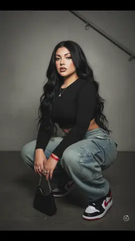 She Got It 🩷  Prompt: A contemporary woman in the style of the late 1990s or early 2000s poses confidently, crouching, in front of a dark, minimalist background that suggests a concrete wall or staircase. She wears a black long sleeve top that exposes her midriff and baggy denim cargo pants. She's wearing black and red Nike sneakers. In her right hand, she holds a small black bag with chain details. Her very long hair falls freely over her shoulders. She wears several rings on her fingers, a red bracelet on her left wrist, and a thin necklace with a small pendant. The lighting is muted, creating a slightly grainy, almost nostalgic atmosphere, like an old flashlight camera. The entire scene has a slightly grainy or grainy effect reminiscent of vintage photography. The makeup is expressive: long black eyelashes, beige and white shadow, strong knees and blush, skin and lips plumped with brown lip gloss and darker brown lip liner. Her eyebrows are well-groomed with Brown Lifting Effect. She has long, well-groomed nails. (Keep her facial features as they are.) #fyp #gemini #prompt #chatgpt #foryoupage 