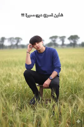 صورة ب الذكاء الاصطناعي برنامج Gemini  الكلام المطلوب: ‏Hyperrealistic editorial portrait of a person sitting on a wooden stool in an open field, facing the camera and looking directly at it. Using the reference image as a STRICT source, preserve the EXACT likeness of the person. This includes EXACT facial features, EXACT natural expression, and EXACT hair. ‏The person wears a thin indigo blue sweatshirt rolled up to the forearms, black pants, and black sneakers. Their posture is relaxed and natural, with one hand resting gently against the side of their head and the other hand resting comfortably on the corresponding knee. ‏The background includes tall grass, sparse trees, and a soft, bright overcast sky. The lighting is clear and diffused daylight, brighter than early morning but without harsh shadows, creating even illumination and natural colors. ‏Lighting: bright, diffused daylight that enhances the textures of skin and fabric without strong contrast. ‏Camera simulation: full-frame camera, 50mm lens, f/2.2 aperture, ISO 200. Shallow depth of field isolates the subject while softly blurring the background. ‏Style: editorial portrait with poetic and minimalist undertones. Evokes quiet reflection and a connection to nature. ‏Color grading: natural and bright with soft contrast. Preserve skin realism while enhancing the clear daylight and the indigo blue of the sweatshirt. ‏Atmosphere: contemplative, clear, and emotionally grounded. ‏editorial portrait, diffused daylight, soft light, natural lighting, shallow depth of field, contemplative, direct gaze --v 6.0 --ar 3:4 --style raw #كربلاء #احمد_عدنان📸 #تصوير #الفيادة #gemini 