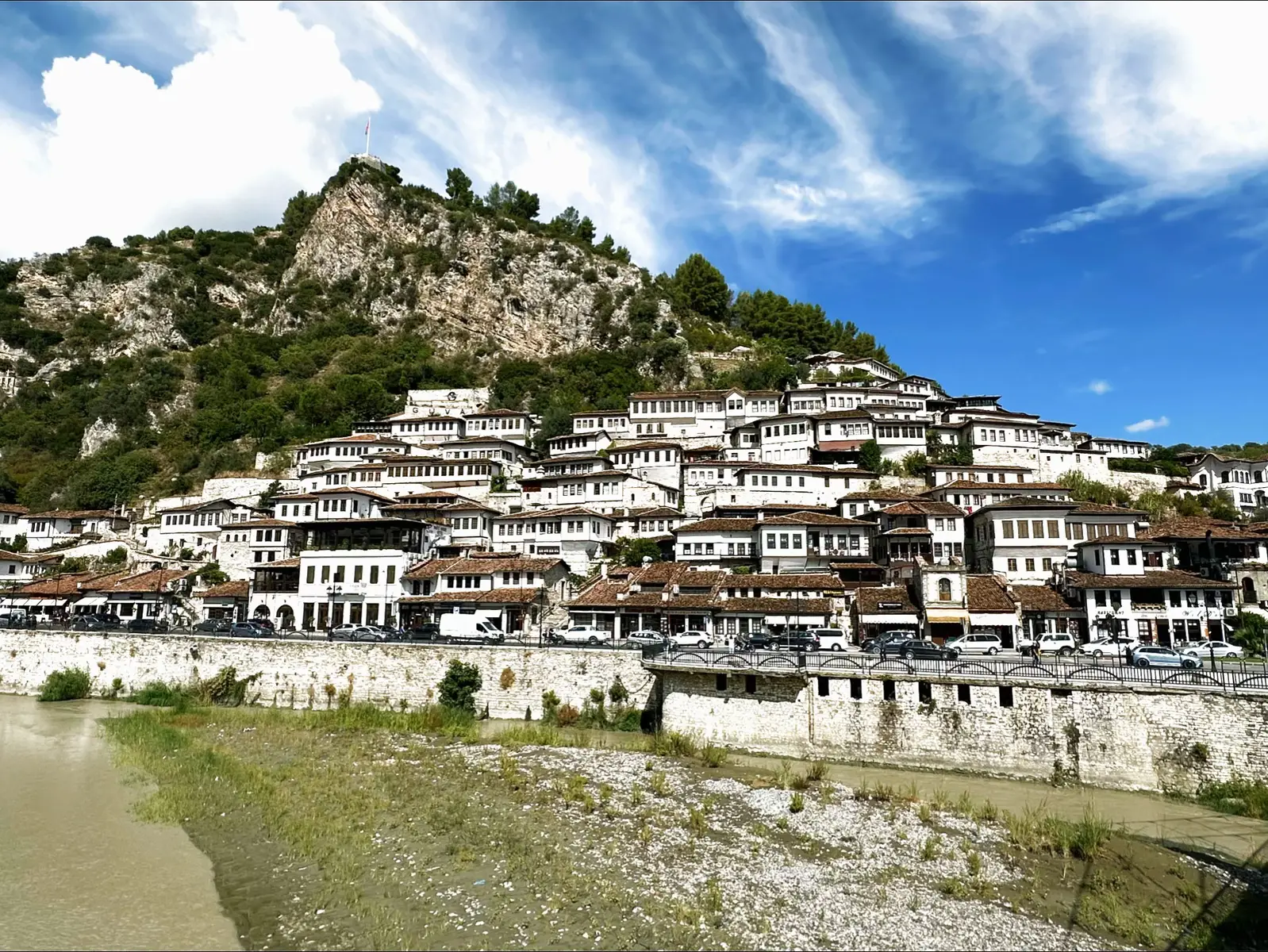 Berat – la coquette aux mille fenêtres Berat, c’est un peu la Mona Lisa des villes : elle te regarde, tu la regardes, et personne ne sait qui drague qui. Ses maisons blanches s’accrochent à la colline comme si elles avaient peur de rater la vue, et son fleuve Osum joue le rôle du miroir romantique. Tu montes au château, tu perds 3 litres d’eau, mais tu gagnes un panorama de carte postale. Et si tu tends l’oreille, la ville te chuchote : « Respire, voyageur. Ici, même les pierres ont pris leur retraite.  Gjirokastër – la dure à cuire en pierre naturelle À deux heures de route, voici Gjirokastër, la sœur badass de Berat. Ici, tout est en pierre : les maisons, les toits, les rues… même les habitants ont un petit air de forteresse. Le château domine la vallée comme un prof de sport en colère, et le vieux bazar t’hypnotise jusqu’à ce que tu repars avec un tapis dont tu n’avais pas besoin. Gjirokastër, c’est pas du charme sucré — c’est du charme à l’ancienne : brut, solide, qui sent la poussière noble et le café fort. En résumé Berat te sourit. Gjirokastër te jauge. Mais les deux te feront tomber amoureux — soit de leur beauté, soit de leurs escaliers (par le genou). #pourtoi💀❤️  #foryoupage❤️  #berat#gjirokaster#albanie💋