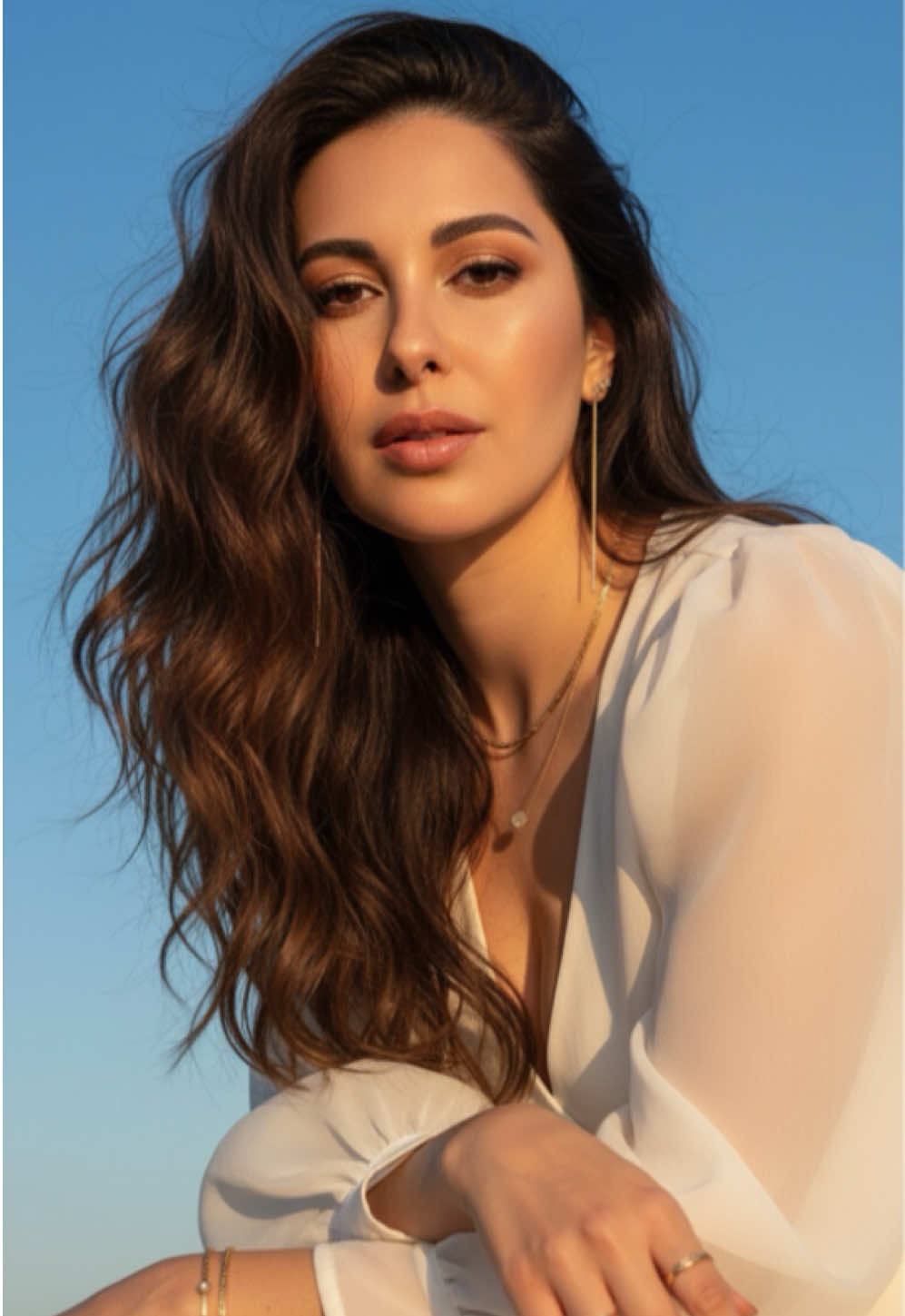 Prompt for Gemini ☀️ ✨ Crie um retrato hiper-realista e cinematográfico inspirado na imagem de referência (FA96B849…), adaptado para um cenário externo com luz natural e atmosfera de editorial de moda. A mulher aparece em close, com o corpo levemente inclinado para frente e o rosto voltado para a câmera, transmitindo um olhar sereno, confiante e envolvente. Ela tem cabelos escuros muito longos, com pontas levemente mais claras, caindo em ondas soltas e naturais, levemente esvoaçantes pela brisa suave. Seus olhos castanhos refletem a luz do sol, com brilho intenso e expressivo. A pele tem textura realista e tom quente, com luminosidade dourada e natural, evidenciando a luz solar suave sobre o rosto, ombros e colo. Ela veste uma blusa branca fluida, com mangas bufantes translúcidas que captam o brilho do sol e refletem suavemente a luz, criando contraste elegante com o fundo azul. Usa acessórios dourados — brincos longos, colar e pulseiras finas e elegantes — que reluzem discretamente sob a luz natural. As mãos da mulher aparecem na imagem, repousando com leveza, exibindo pulseiras e dois anéis dourados, que reforçam o toque sofisticado e natural da cena. O fundo mostra um céu azul intenso e limpo, com tons quentes de sol refletindo de forma suave e cinematográfica. A iluminação é solar e dourada, com sombras delicadas e brilho difuso, realçando o volume do cabelo, a textura da pele e o tecido leve da roupa. A composição deve transmitir beleza natural, elegância e realismo vívido, com qualidade 8K ultrarrealista, alta nitidez, textura detalhada e atmosfera editorial de moda ao ar livre, mantendo a essência da pose, expressão e estilo originais da referência. #prompts #gemini #artificialintelligence #chatgpt #ia 